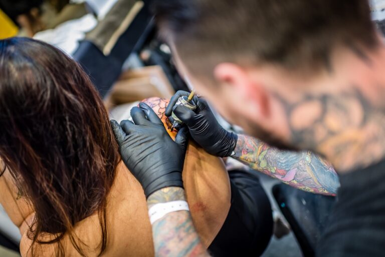 Tattoo artist in black gloves tattooing a client's shoulder