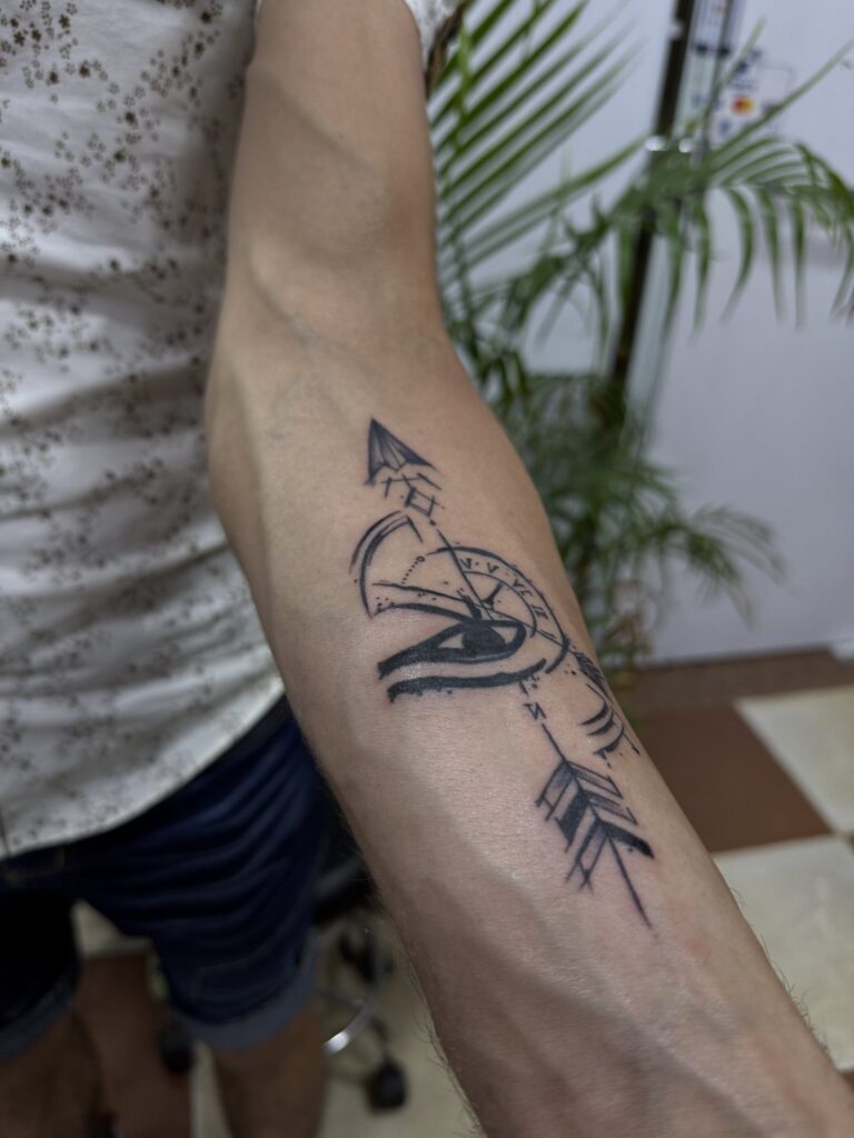 Arrow and Eye of Horus forearm tattoo – black and grey linework