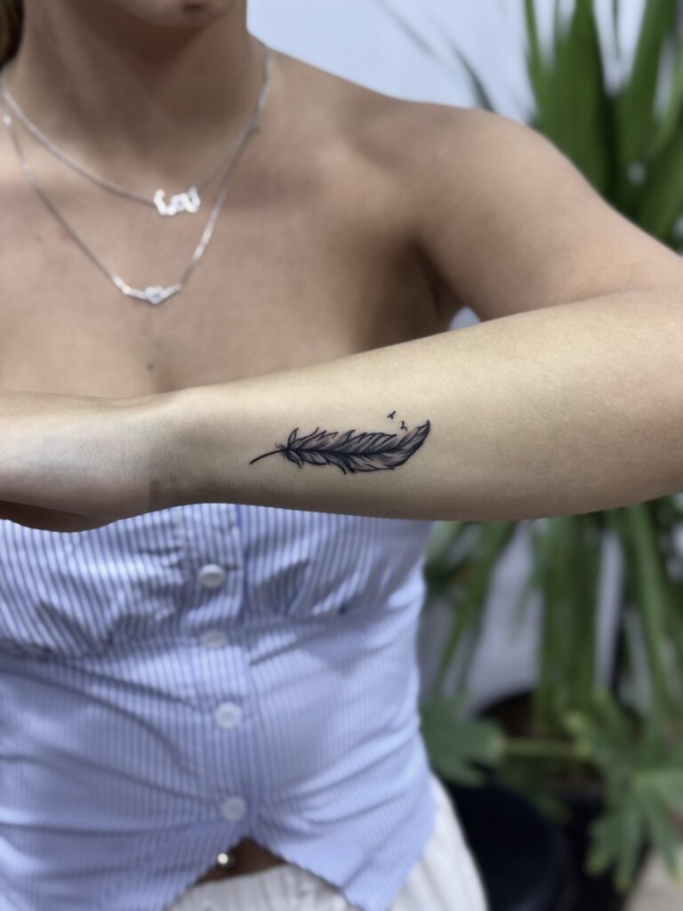 Fine line feather tattoo on forearm