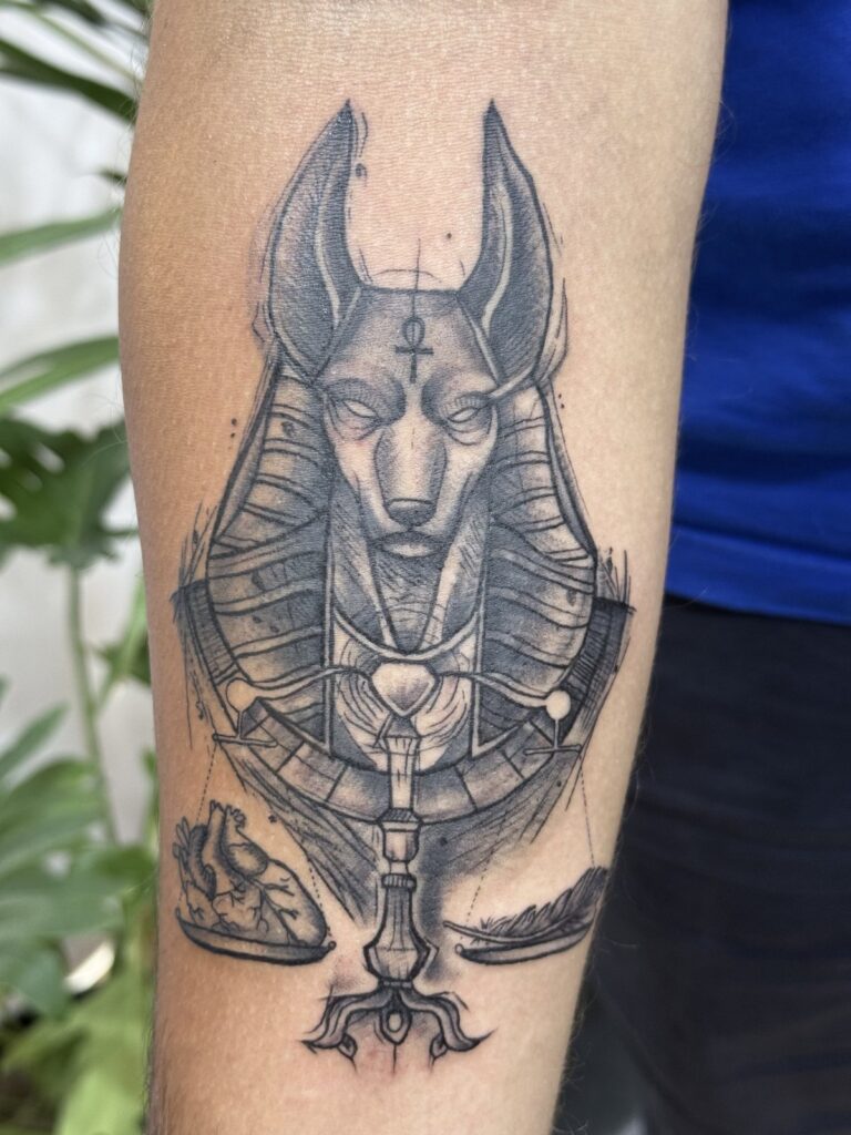 Anubis head black and grey forearm tattoo with ornamental details
