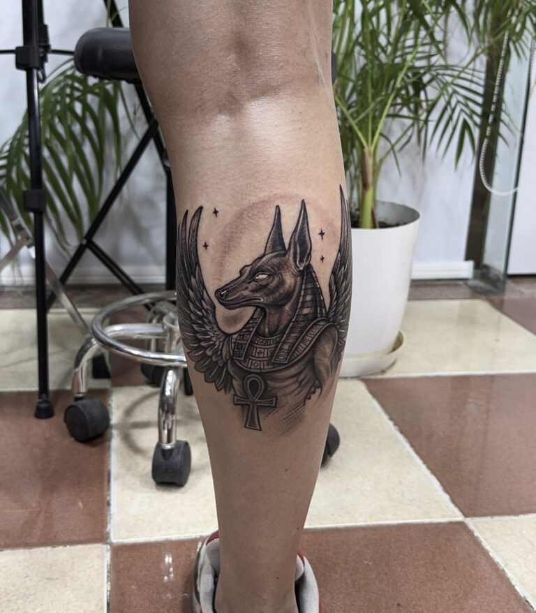 Winged Anubis tattoo with ankh on calf – Egyptian black and grey tattoo Hurghada
