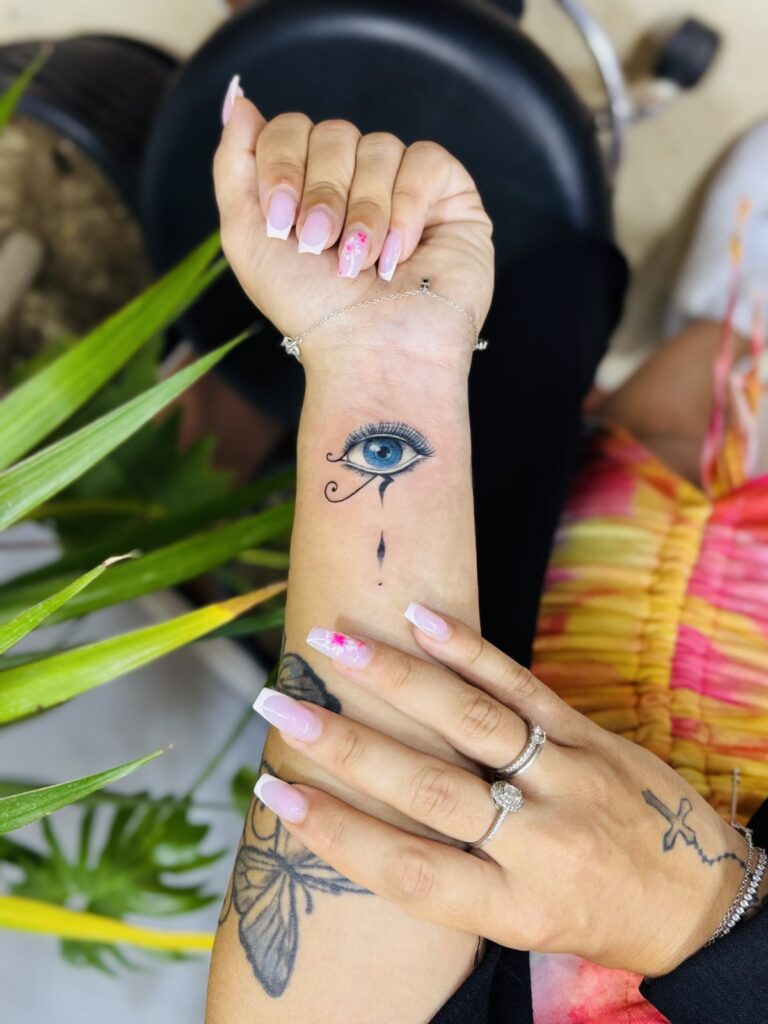 Blue evil eye fine line wrist tattoo with color accent