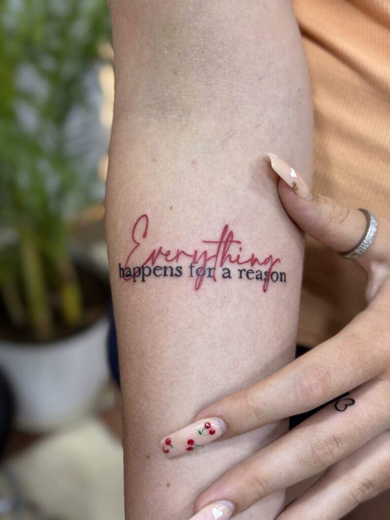 Everything happens for a reason script tattoo with red lettering on forearm