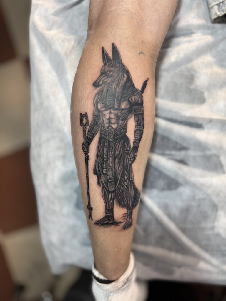 Anubis warrior figure tattoo on forearm – Egyptian black and grey realism
